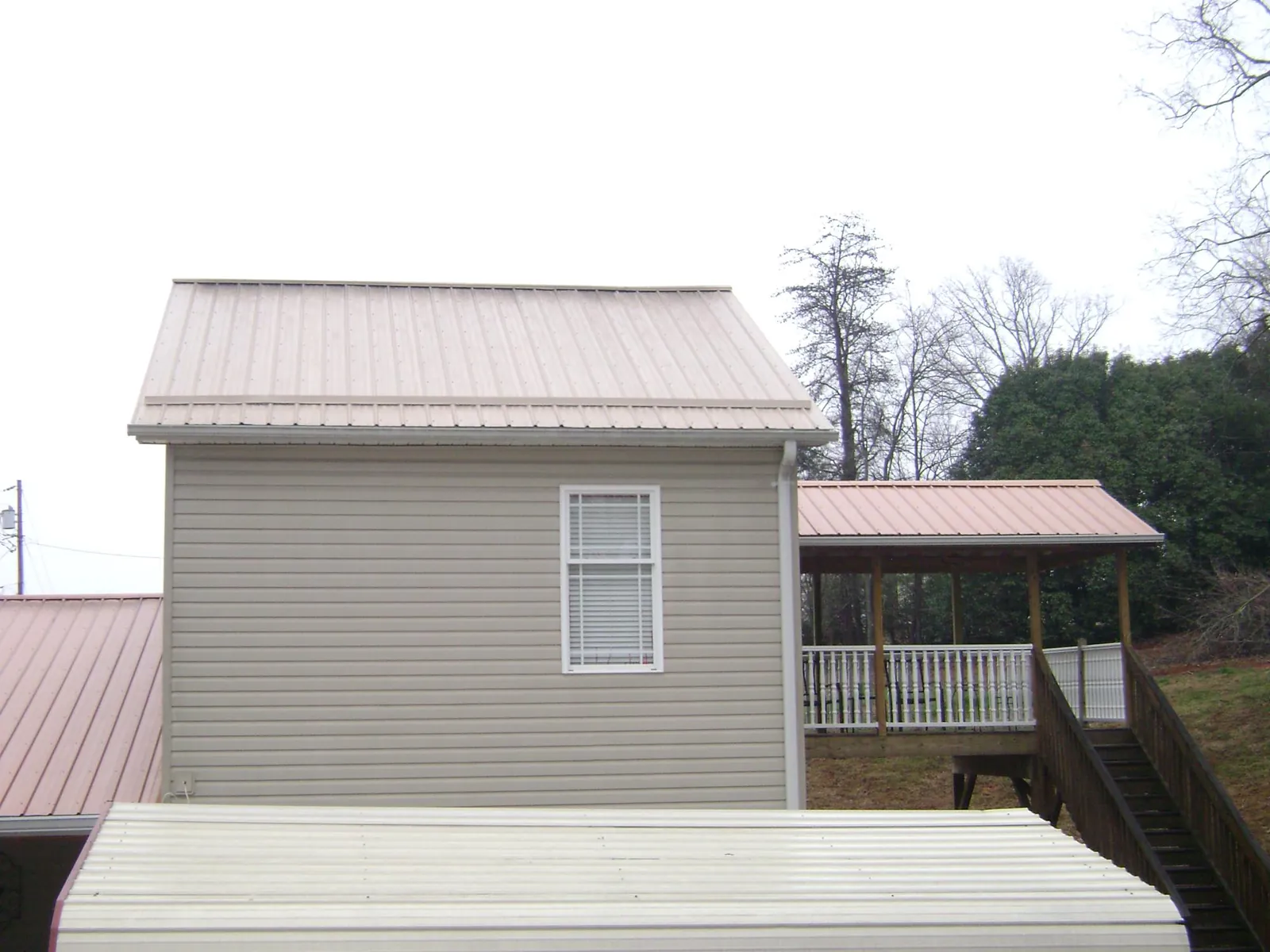 Tan metal roofs on a two story addition and attached porch, from a Roof Replacement job in West Point